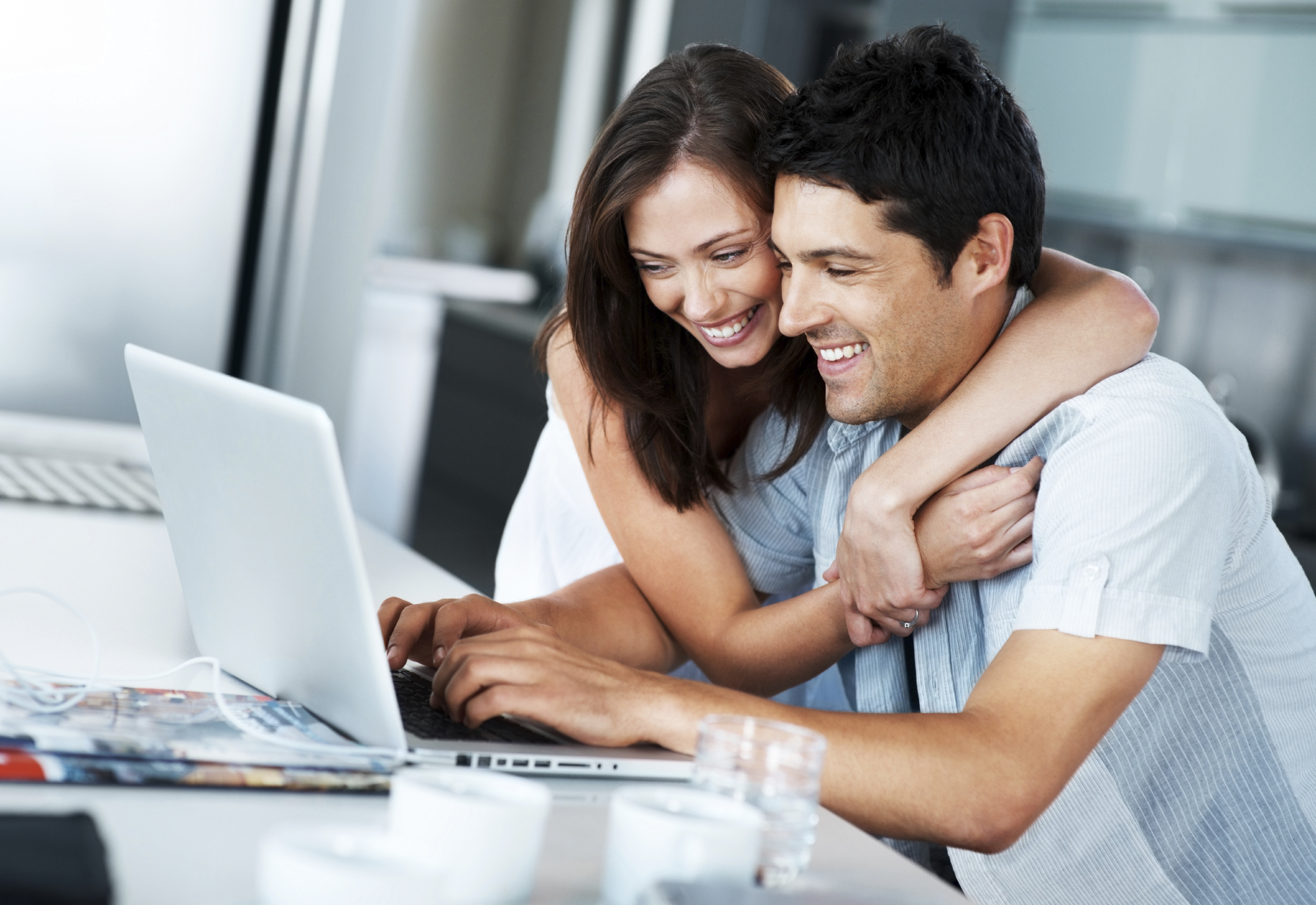 Portrait of a smiling young couple surfing internet on laptop in kitchen at home